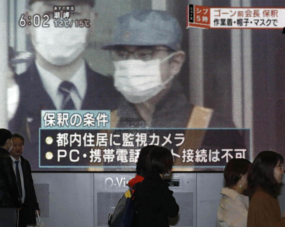 People walk by a monitor which reports on the bail of former chairman of Nissan Motor Co., Carlos Ghosn, in Osaka, western Japan Wednesday, March 6, 2019. Disguised as a construction worker, Ghosn left a Tokyo detention center Wednesday after posting 1 billion yen ($8.9 million) bail. The letters, bottom, read " Conditions for his release." (Kyodo News via AP)