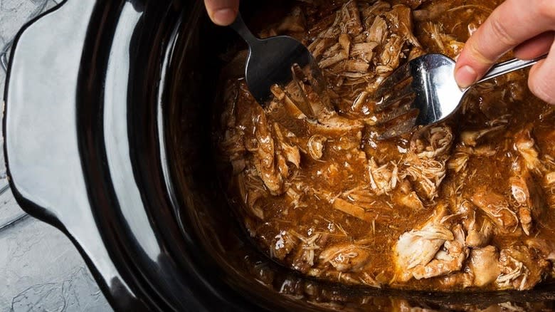 Forks shredding chicken in pot