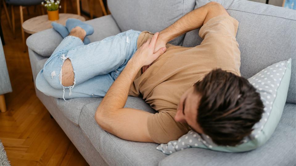 young man lying on a couch holding his right lower abdomen as if in pain