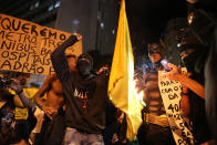 Masked demonstrators set fire to a jersey with the colors of Brazilian national soccer team during protest against the World Cup 2014, in Rio de Janeiro, Brazil, Thursday, March 27, 2014. Demonstrators call for better schools, health care, questioning the billions spent to host this year's World Cup and the 2016 Olympics. (AP Photo/Leo Correa)