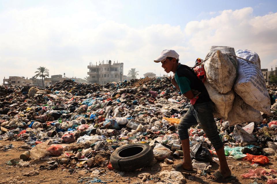 A Palestinian youth carries sacks of salvageable items past piles of waste as garbage collection and any other municipality services come to a halt due to the Israeli bombardment of the Gaza Strip.