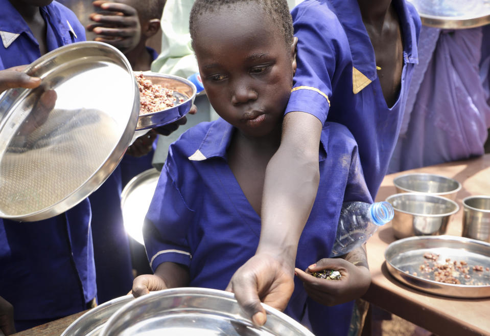 In this photo taken Tuesday, March 26, 2019, children push their plates out to receive a portion of cooked grains during a lunchtime feeding program initiative launched by UNICEF and the World Food Programme with the aim of providing daily meals to 75,000 children in Aweil, Northern Bahr el Ghazal state, in South Sudan. Human rights activist Mia Farrow spoke to The Associated Press as she visited South Sudan again in her new role as envoy for the International Rescue Committee, helping the aid group to promote a global initiative to change the way humanitarian organizations approach malnutrition. (AP Photo/Sam Mednick)