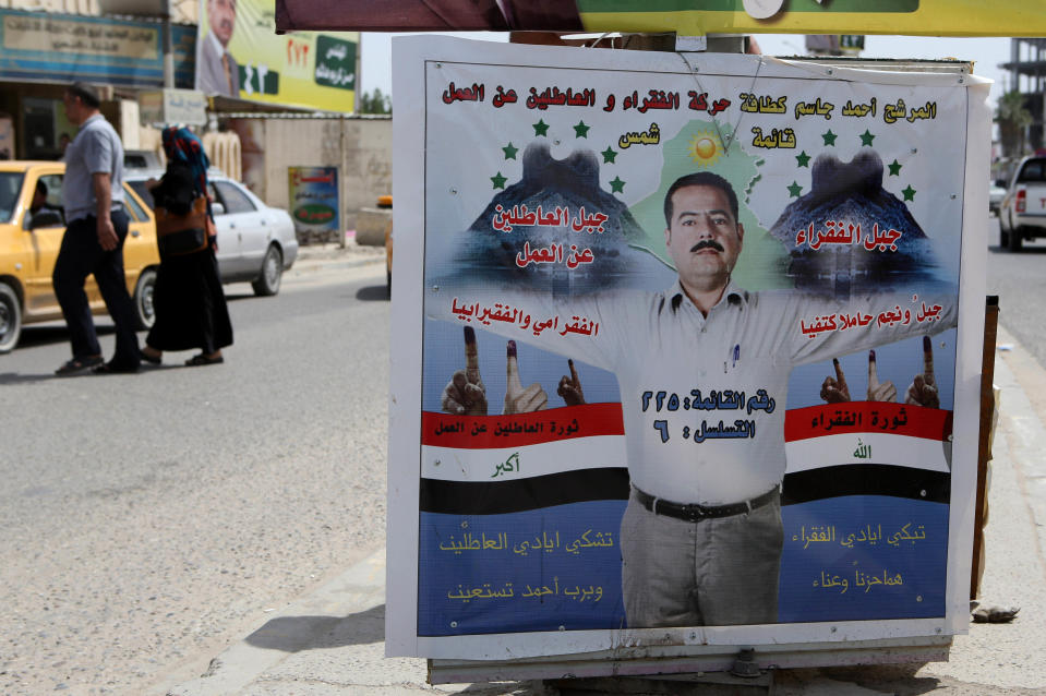 In this photo taken on April 15, 2014, Iraqis pass by an election poster depicting parliamentary candidate, Ahmed Jassim, stretching his hands and bearing two mountains, one for jobless people and another for poor people, in a gesture suggesting that he will bear the burden for their suffering. Jassim represents the Movement of the Poor and Jobless People in Basra, Iraq. Iraqis are united on one conclusion that there is dim hope this election will bring real change and better days for them. (AP Photo/Nabil al-Jurani)