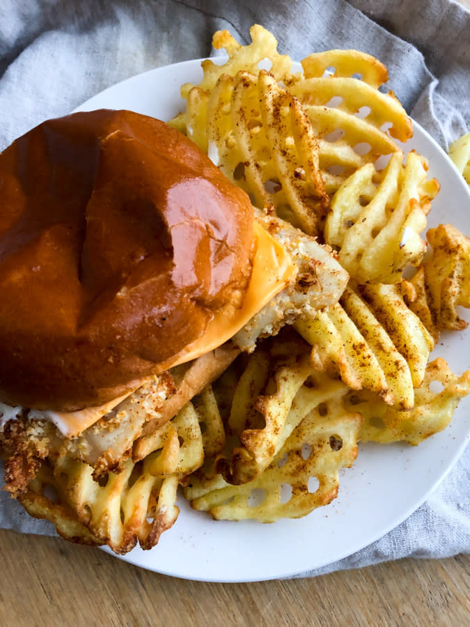 A bun filled with a crispy fish fillet and fries on the side.