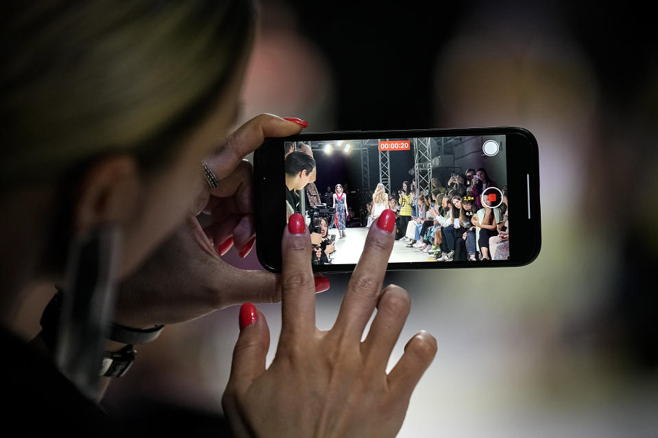 A spectator films on her smartphone as models display a collection by Russian designer Polina Mircheva during the Fashion Week at Zaryadye Park near Red Square in Moscow, Russia, Wednesday, June 22, 2022. (AP Photo/Alexander Zemlianichenko)