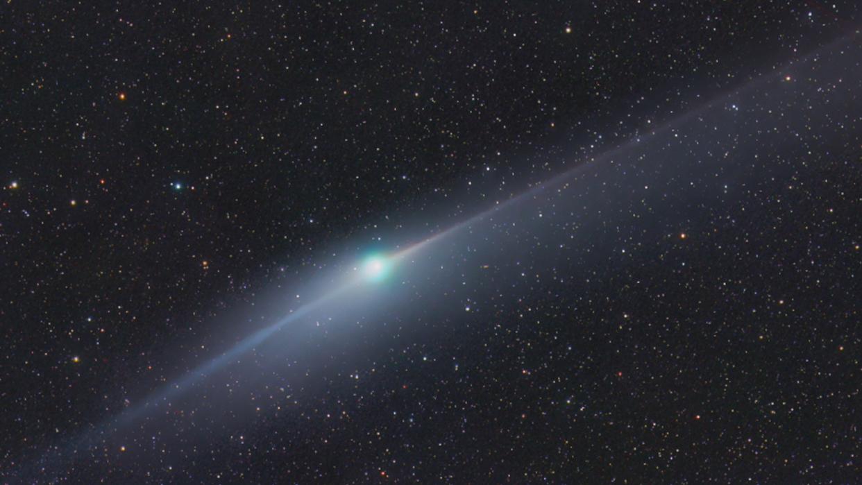  A green comet in space with two long tails of light stretching in opposite directions. 