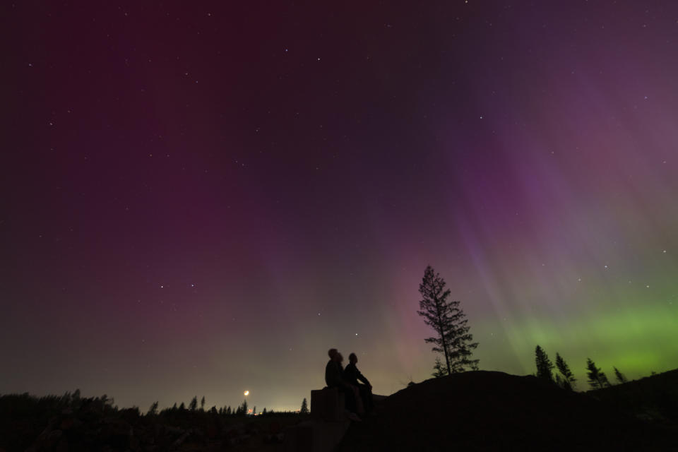 In this image taken with a long exposure, people look at the night sky towards the northern lights, or Aurora Borealis, on Friday, May 10, 2024, in Estacada, Ore. The National Oceanic and Atmospheric Administration issued a rare severe geomagnetic storm warning when a solar outburst reached Earth on Friday afternoon, hours sooner than anticipated. The effects were due to last through the weekend and possibly into next week. (AP Photo/Jenny Kane)