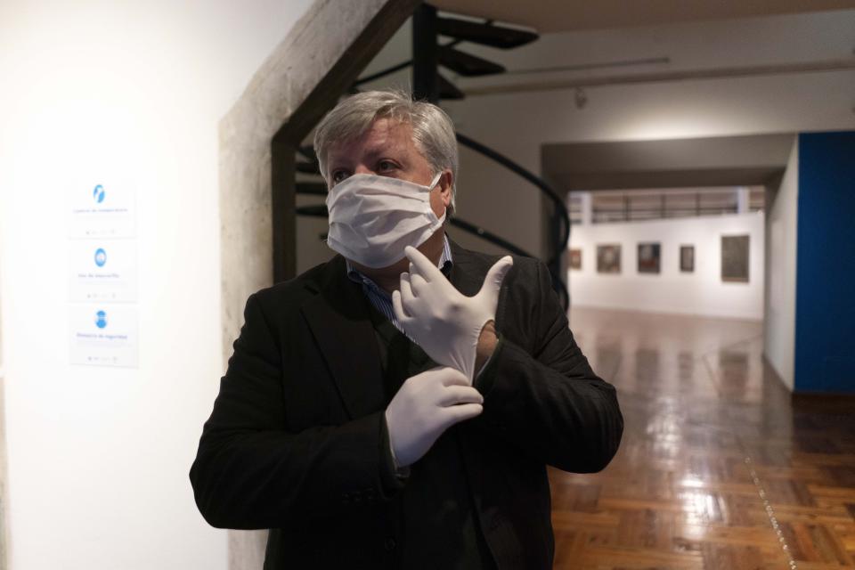 Wearing a face mask and plastic gloves amid the spread of new coronavirus, Enrique Aguerre, director of the National Museum of Visual Arts, waits for visitors on the second-day of reopening the museum in Montevideo, Uruguay, Tuesday, Aug. 4, 2020. After more than four months closed due to restrictions to curb the spread of COVID-19, movie houses, museums and theaters re-opened nationwide on Monday, with social distancing protocols. (AP Photo/Matilde Campodonico)