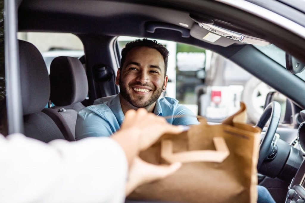 A man delivers food to a person while sitting in his car. 