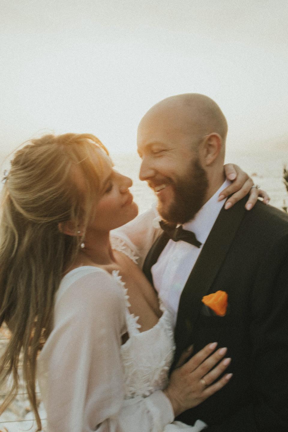 A bride and groom look at each other and smile as they hug.