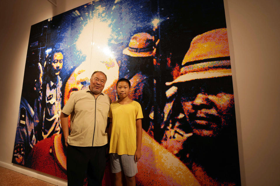 Chinese artist Ai Weiwei poses with his son Lao (13) in front of a self portrait made by lego at the San Giorgio deconsecrated church in Venice, Italy, Friday, Aug. 26, 2022. Chinese artist Ai Weiwei lampoons the surveillance culture and social media with his first ever glass sculpture, made on the Venetian island of Murano, that stands as a warning to the world: "Memento Mori,'' or Latin for "Remember You Must Die." (AP Photo/Luca Bruno)
