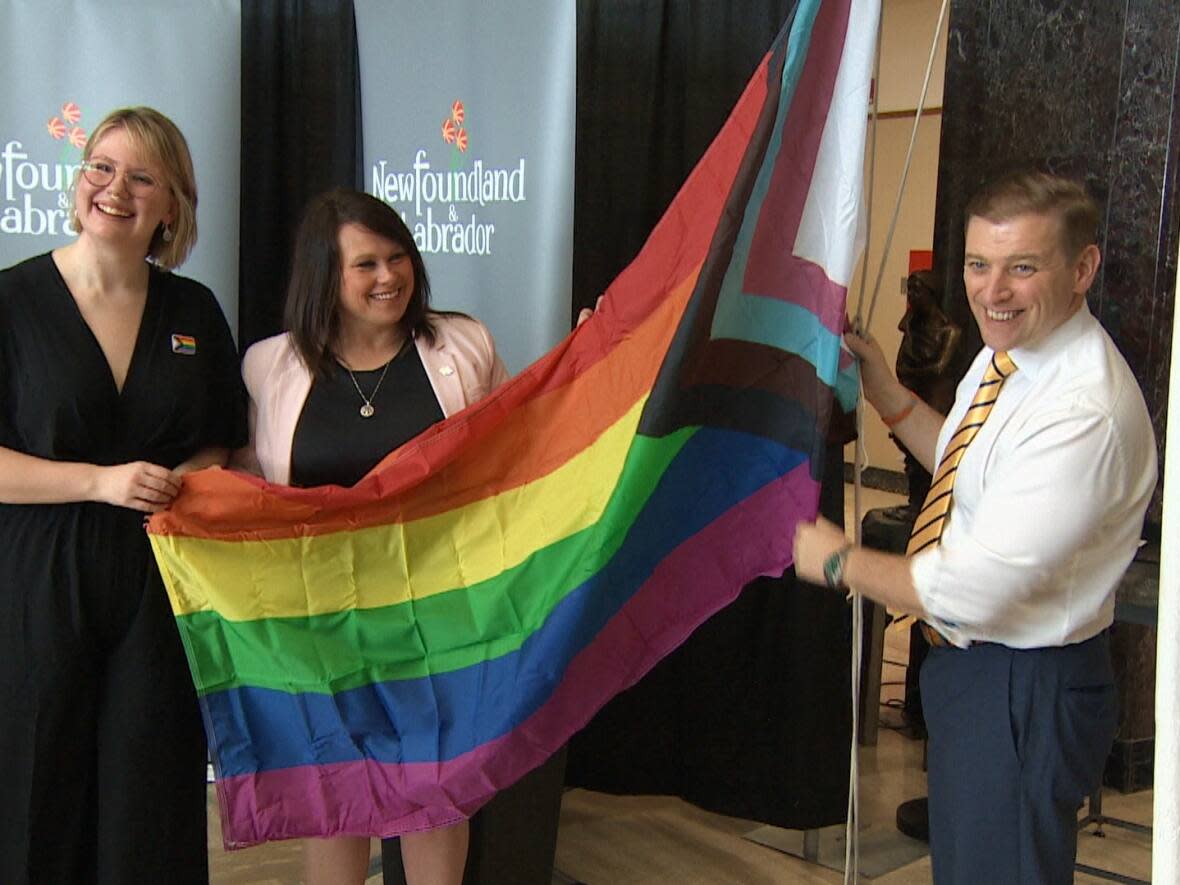 From left: Sarah Worthman of the N.L. Queer Research Initiative, Gender Equality Minister Pam Parsons and Premier Andrew Furey raise the Progress Pride flag at Confederation Building on Thursday. (Darryl Murphy/CBC - image credit)