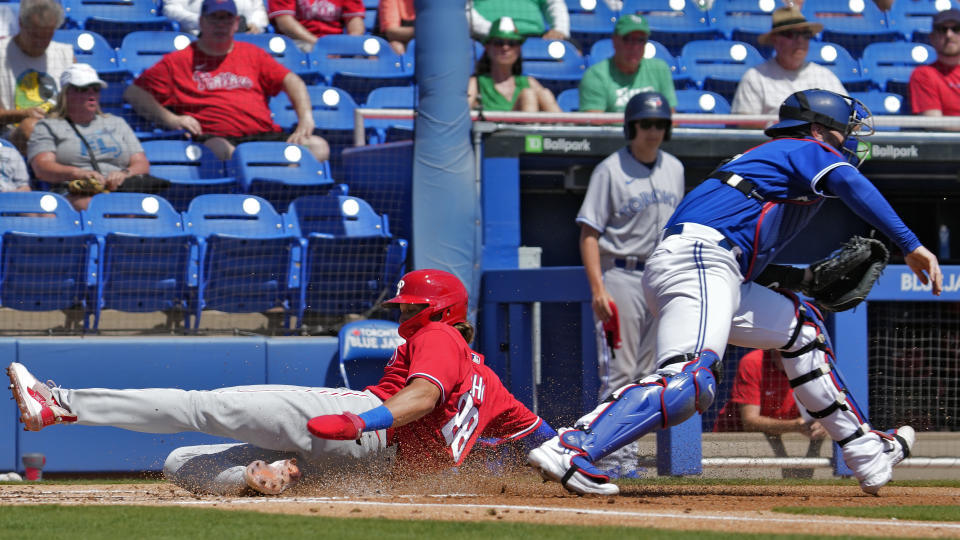 Philadelphia Phillies' Alec Bohm (28) scores past Toronto Blue Jays catcher Danny Jansen on a sacrifice fly by Josh Harrison during the first inning of a spring training baseball game Friday, March 17, 2023, in Dunedin, Fla. (AP Photo/Chris O'Meara)