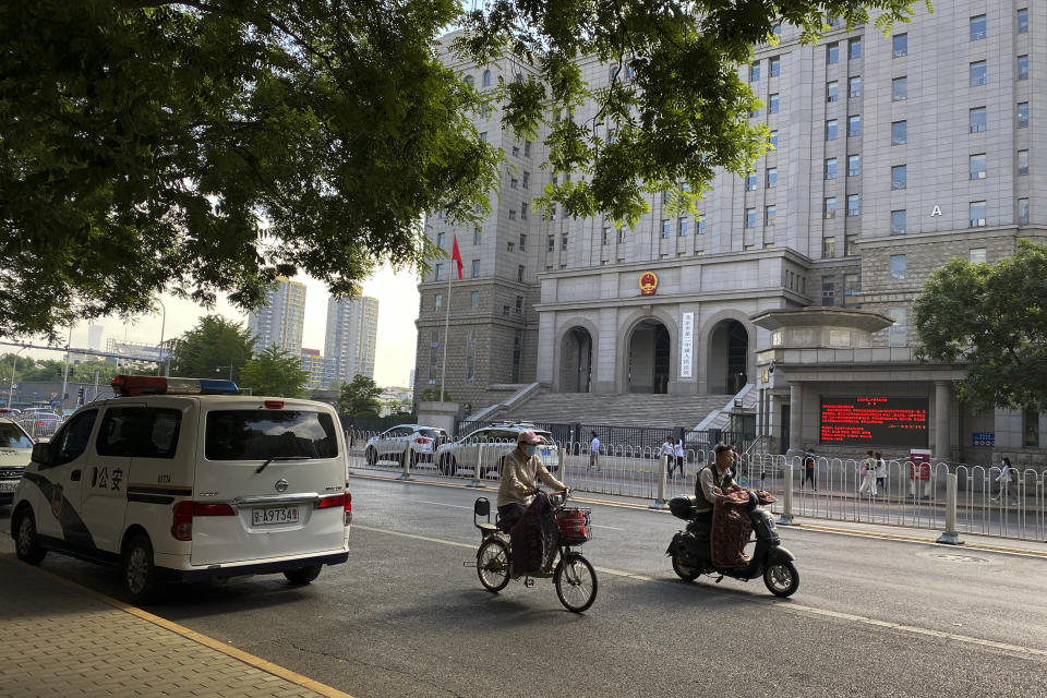 People ride scooters passing by a police van parked near the No. 2 Intermediate People's Court where the espionage charges case for Yang Hengjun is going to be held in Beijing, Thursday, May 27, 2021. Australian ambassador to China Graham Fletcher said it was “regrettable” that the embassy was denied access Thursday as a trial was due to start for Yang, a Chinese Australian man charged with espionage. (AP Photo/Andy Wong)