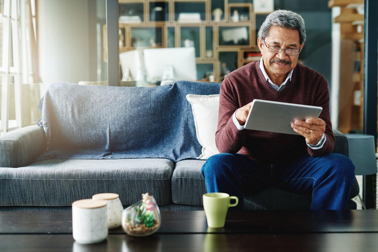 Cropped shot of a mature man using his digital tablet while relaxing at home