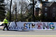 A police officer walks past a Boston Strong banner as Wellesley College students affix the banner to the barricades before the start of the 118th Boston Marathon Monday, April 21, 2014 in Wellesley, Mass. (AP Photo/Mary Schwalm)