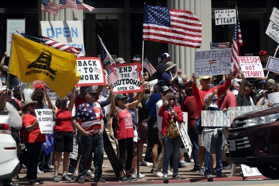 People hold signs and flags during a protest against measures aimed at slowing the spread of the new coronavirus Friday, May 1, 2020, in San Diego. (AP Photo/Gregory Bull)