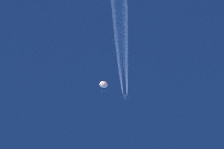 In this photo provided by Brian Branch, a large balloon drifts above the Kingstown, N.C. area, with an airplane and its contrail seen below it. The United States says it is a Chinese spy balloon moving east over America at an altitude of about 60,000 feet (18,600 meters), but China insists the balloon is just an errant civilian airship used mainly for meteorological research that went off course due to winds and has only limited “self-steering” capabilities.