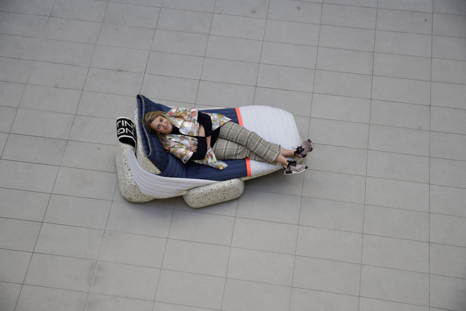 In this picture taken on Wednesday, April 17, 2019, designer Patricia Urquiola relaxes sitting on her creation 'Wasting Time Daybed' made from upcycled plastic for the "RO Plastic - Master's Pieces" exhibition, on the sidelines of Milan's Furniture Fair, in Milan, Italy. Scientists and environmental activists have been long raised the alarm on plastic pollution. Now, the high-end design world is getting in on the growing global effort to tackle plastic pollution -- by upcycling discarded objects into desirable one-off design pieces. (AP Photo/Luca Bruno)