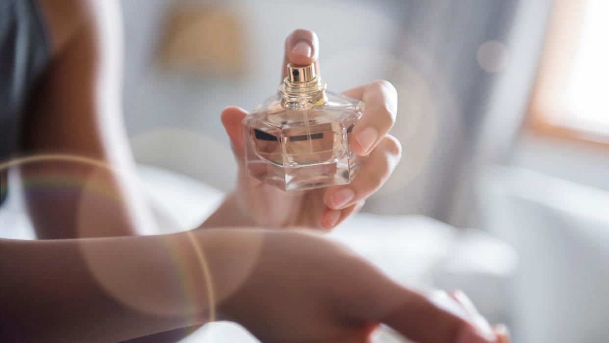  A woman spraying perfume on her wrist to illustrate winter perfume layering. 