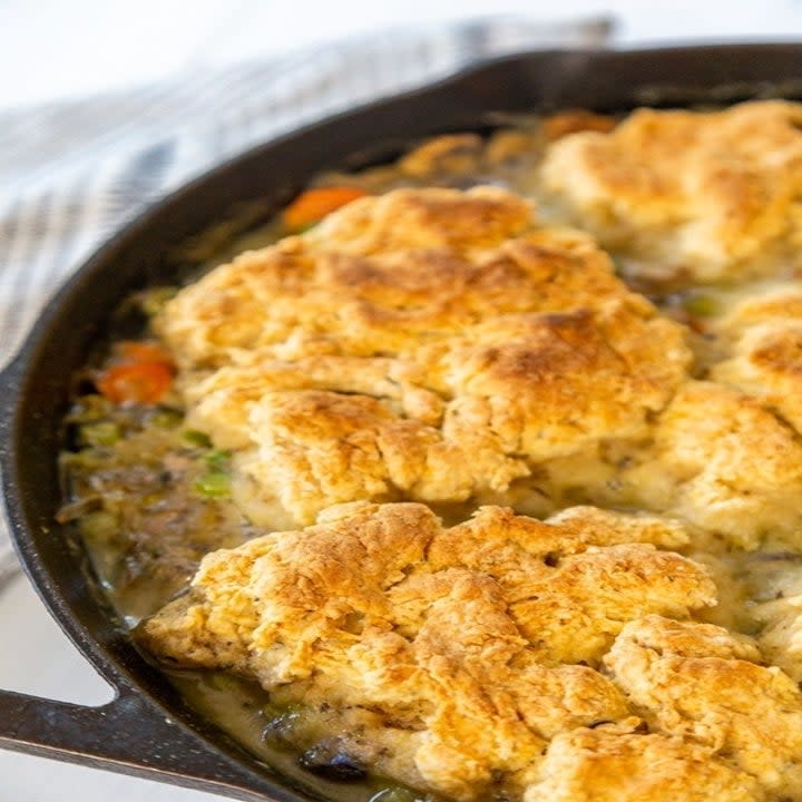 A pan with biscuits on top of chicken and gravy, cooking