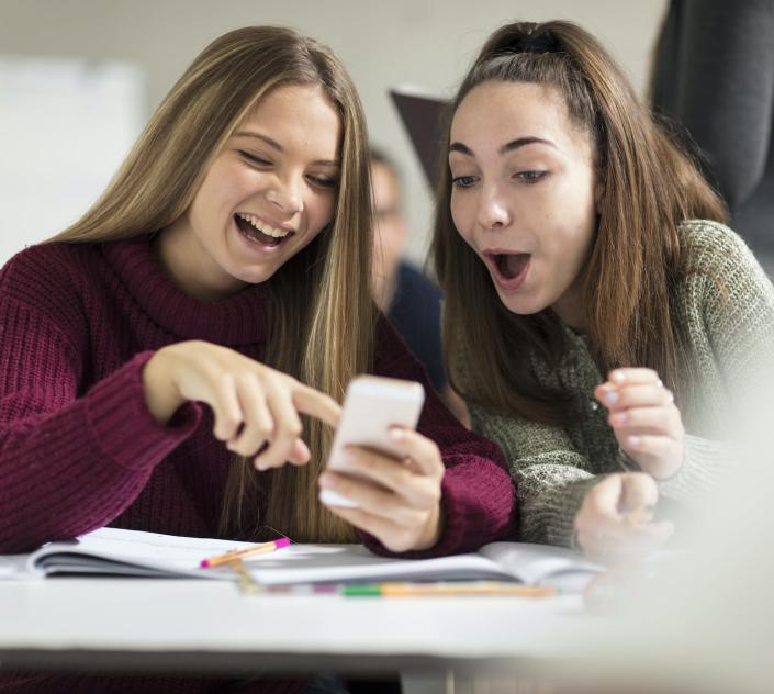 Academic performance improves when schools ban smartphones, research shows. <a href="https://www.gettyimages.com/detail/photo/happy-teenage-girls-in-class-looking-at-cell-phone-royalty-free-image/1011461988?phrase=smartphones+classrooms&adppopup=true" rel="nofollow noopener" target="_blank" data-ylk="slk:Westend61 via Getty Images;elm:context_link;itc:0" class="link ">Westend61 via Getty Images</a>