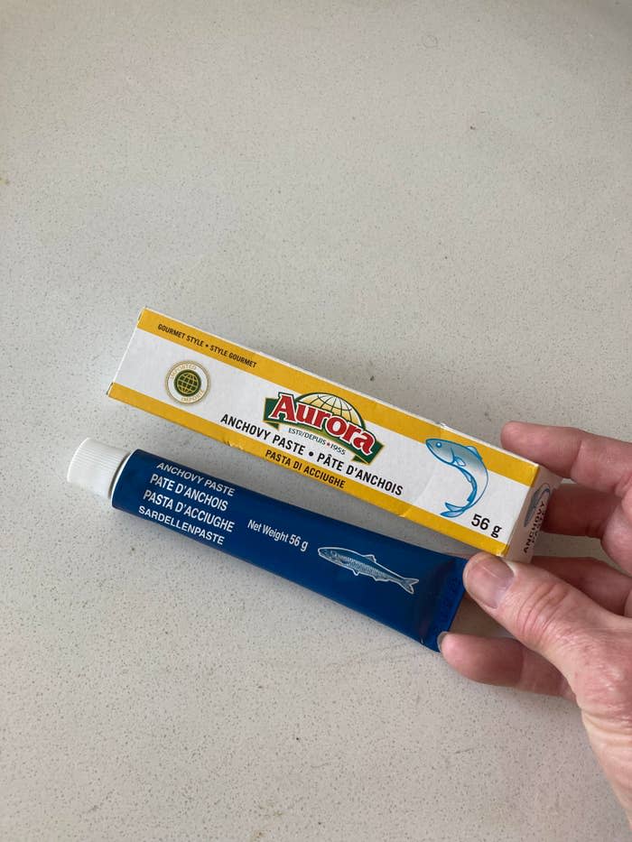 Hand holding a tube of Aurora anchovy paste over a kitchen counter