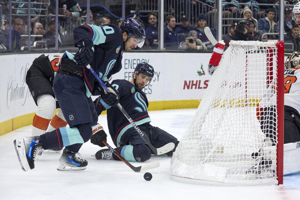 Seattle Kraken center Matty Beniers, front and left wing Tomas Tatar (90) kneeling on the ice, try to control the puck against the Philadelphia Flyers during the first period of an NHL hockey game, Friday, Dec. 29, 2023, in Seattle. (AP Photo/John Froschauer)