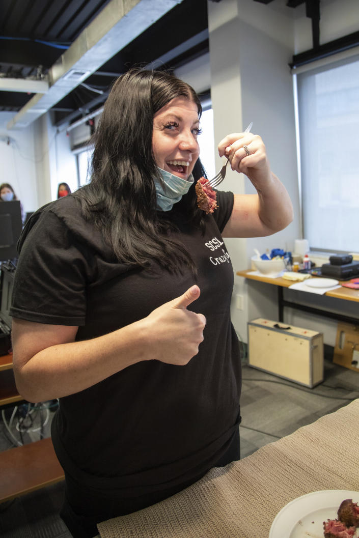 In this photo provided by UPMC and Pitt Health Sciences, research participant Heather Rendulic cuts and eats a piece of steak for the first time since recovering from a series of strokes in 2012, at Pitt's Rehab Neural Engineering Lab in Pittsburgh on June 6, 2021. A stroke left Rendulic with little use of her left hand and arm, so she volunteered for a first-of-its-kind experiment that stimulates her spinal cord in spots that control upper limb motion. (Tim Betler/UPMC and Pitt Health Sciences via AP)