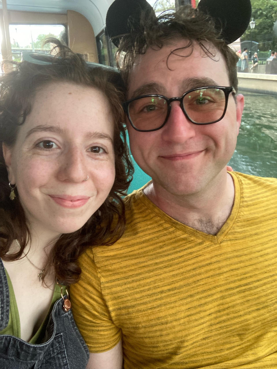 Two happy, smiling people. One wears overalls, the other a yellow shirt and mickey mouse ears.