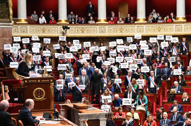 Miembros del grupo parlamentario de la Asamblea Nacional La France Insoumise (LFI) y de la coalición de izquierdas NUPES (Nueva Unión Ecológica y Social de los Pueblos) sostienen carteles en los que se lee "64 es un no", "Nos vemos en la calle" tras la votación de dos mociones de censura en la Asamblea Nacional francesa, el 20 de marzo de 2023.