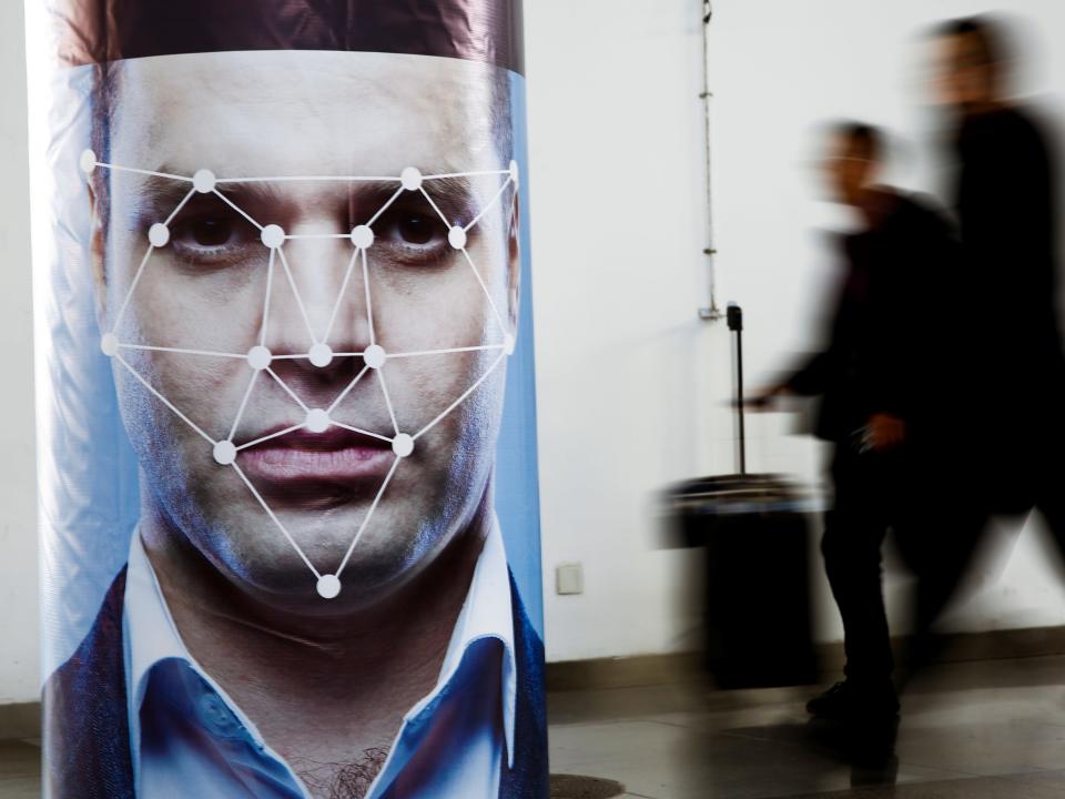 People walk past a poster simulating facial recognition software at the Security China 2018 exhibition