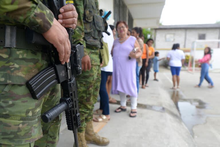 Soldados están de guardia mientras las personas hacen fila para votar en un centro de votación durante un referéndum sobre medidas más estrictas contra el crimen organizado en Olón, provincia de Santa Elena, Ecuador, el 21 de abril de 2024.