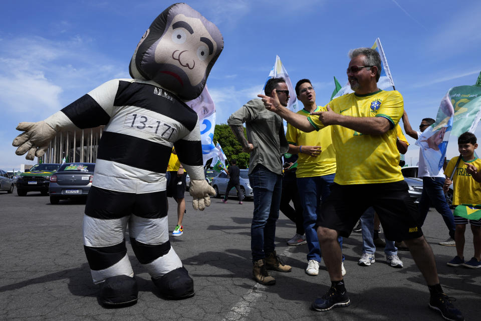 A supporter of Brazil's President Jair Bolsonaro points finger-gun gestures at a giant inflatable doll depicting former President Luiz Inacio Lula da Silva in a prison uniform, during a campaign event in Brasilia, Brazil, Saturday, Oct. 29, 2022. Bolsonaro and da Silva are facing off in a runoff election set for Oct. 30. (AP Photo/Eraldo Peres)