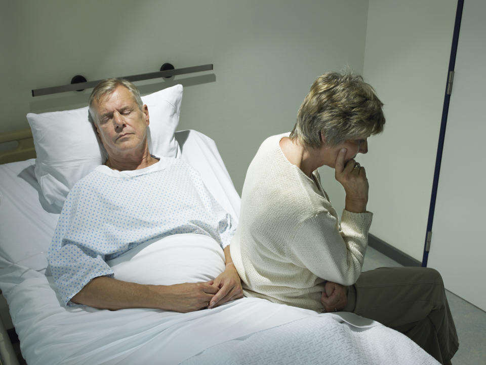 A man lying in a hospital bed and a woman sitting on it and turned away from him