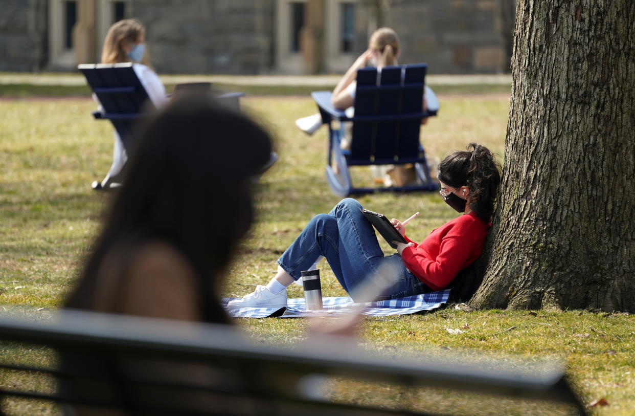 Masked to protect against COVID-19, a Georgetown University student joins others taking advantage of the warm sunshine to study outdoors March 9, 2021. REUTERS/Kevin Lamarque