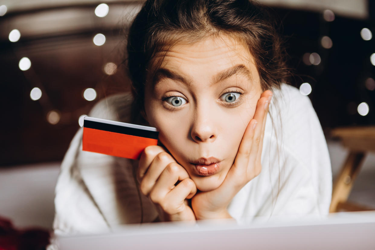 Teen girl is has a facial expression of awestruck while viewing a shopping site online and holding a credit card in one of her two hands at her chin.