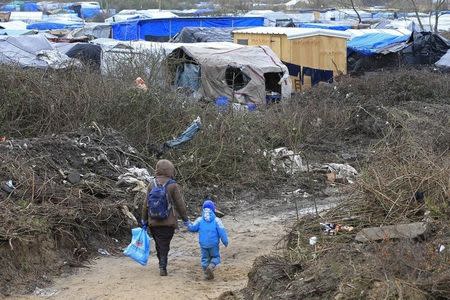 A migrant and her child walk in the southern part of a camp for migrants called the "jungle", in Calais, northern France, February 25, 2016. REUTERS/Pascal Rossignol