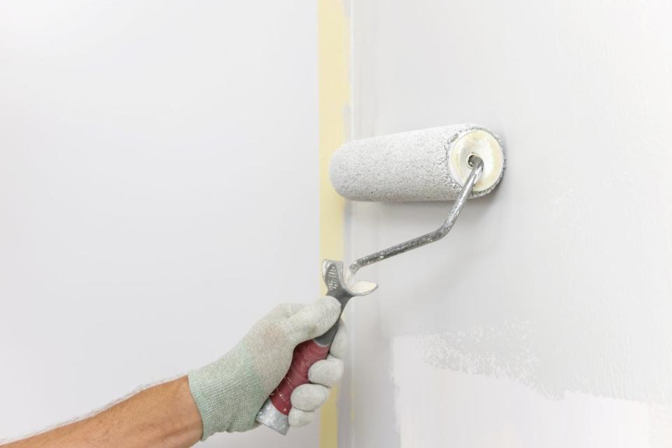 Gloved hand using roller to paint wall