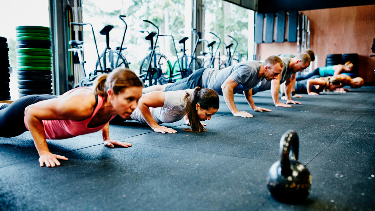  Row of people doing push-ups in gym. 