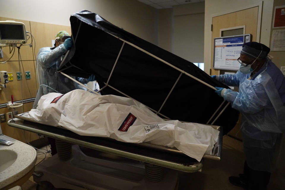 Transporters Miguel Lopez, right, Noe Meza prepare to move a body of a COVID-19 victim to a morgue at Providence Holy Cross Medical Center in the Mission Hills section of Los Angeles Saturday, Jan. 9, 2021. (AP Photo/Jae C. Hong)
