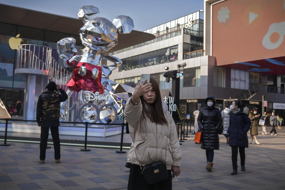 A woman takes a selfie as visitors wearing face masks tour past an outdoor shopping center displaying a Mickey Mouse statue commemorating the Disney 100th anniversary, in Beijing, Thursday, Jan. 5, 2023. As COVID-19 rips through China, other countries and the WHO are calling on its government to share more comprehensive data on the outbreak, with some even saying many of the numbers it is reporting are meaningless. (AP Photo/Andy Wong)