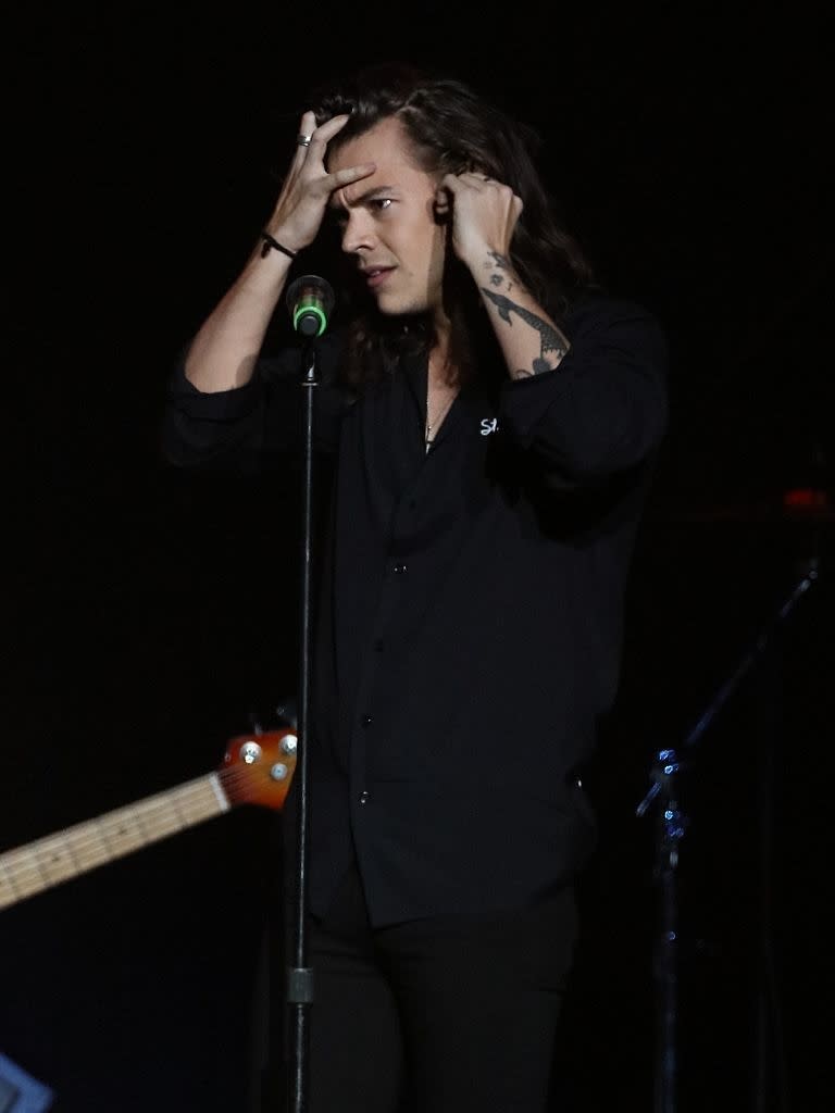 Harry on stage with microphone, adjusting hair