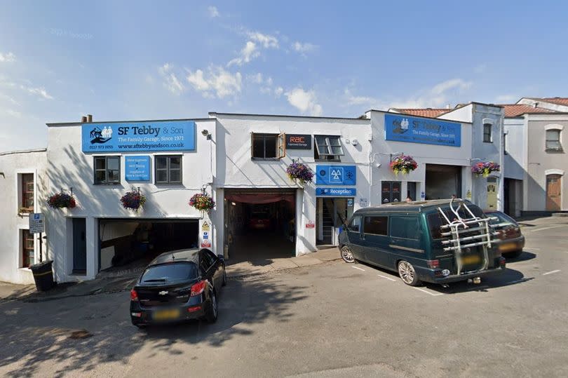 General view of car servicing garage with roller-shutters open and cars parked outside