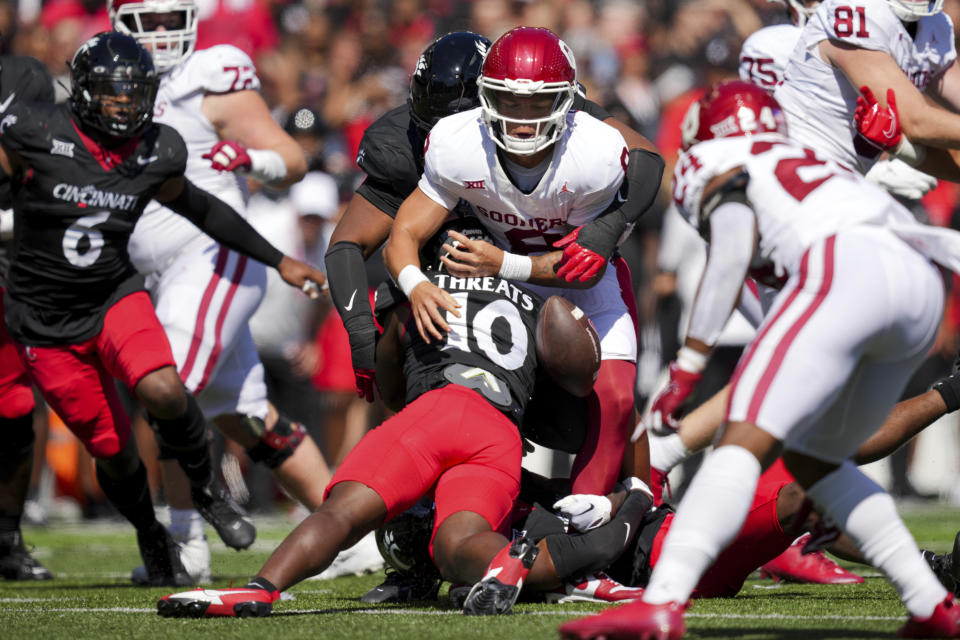 Oklahoma quarterback Dillon Gabriel, center, fumbles the ball as he is tackled by Cincinnati safety Bryon Threats, bottom, and defensive tackle Jalen Hunt, back, during the first half of an NCAA college football game, Saturday, Sept. 16, 2023, in Cincinnati. (AP Photo/Aaron Doster)