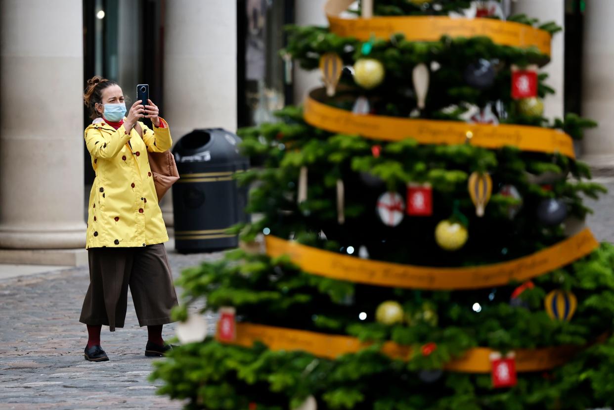 A pedestrian wearing a face mask or covering due to the COVID-19 pandemic takes a photograph of Christmas trees in Covent Garden in central London on November 17, 2020. - Britain has been the worst-hit nation in Europe recording more than 50,000 coronavirus deaths from some 1.2 million positive cases. (Photo by Tolga Akmen / AFP) (Photo by TOLGA AKMEN/AFP via Getty Images)