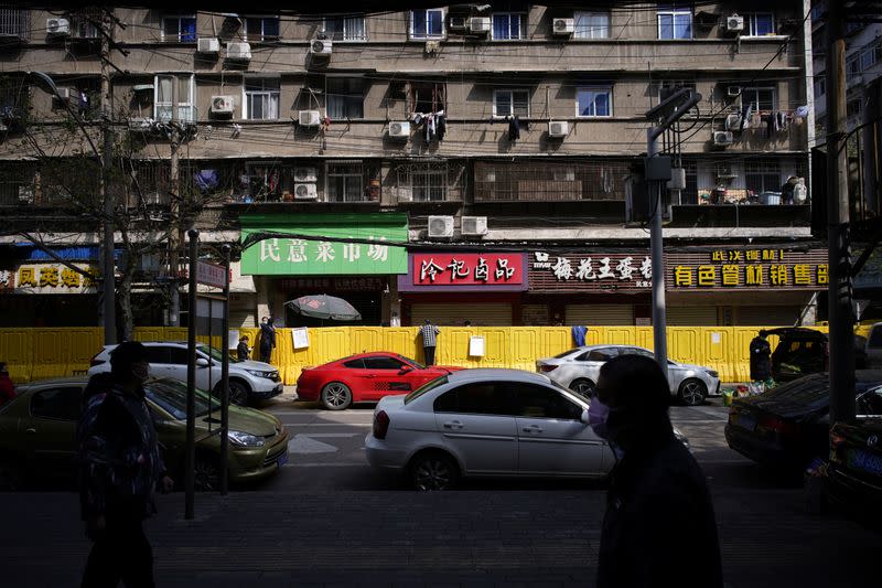 Residents pay for groceries by standing on chairs to peer over barriers set up to ring fence a wet market on a street in Wuhan