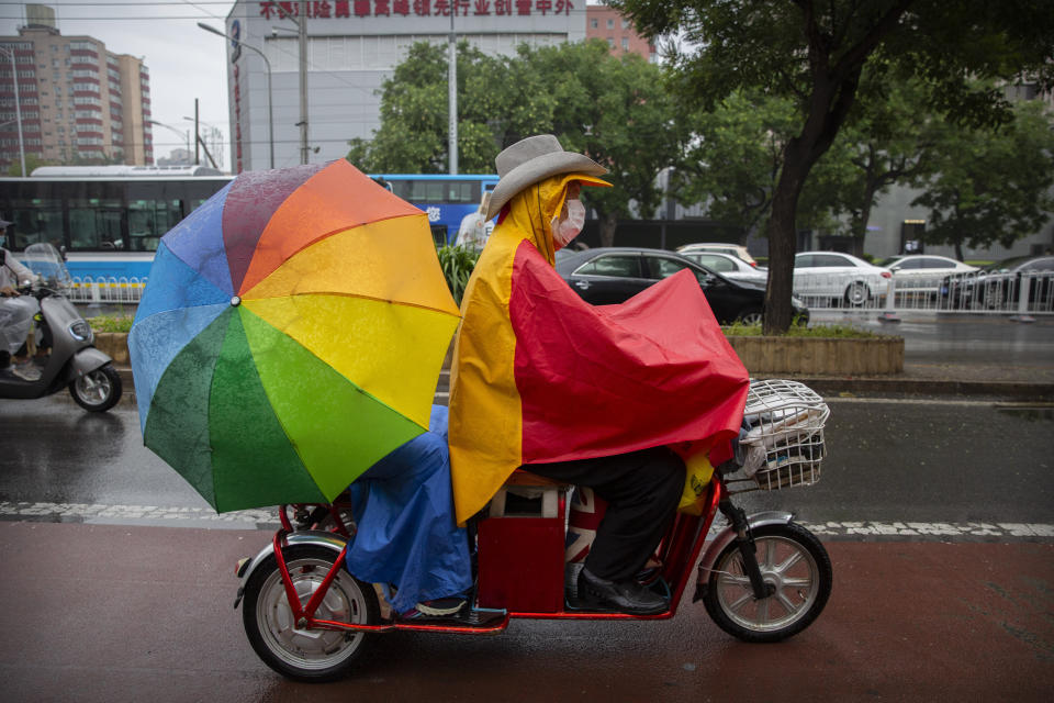 A man wearing a face mask to protect against the spread of the new coronavirus rides a scooter in the rain in Beijing, Thursday, July 9, 2020. (AP Photo/Mark Schiefelbein)