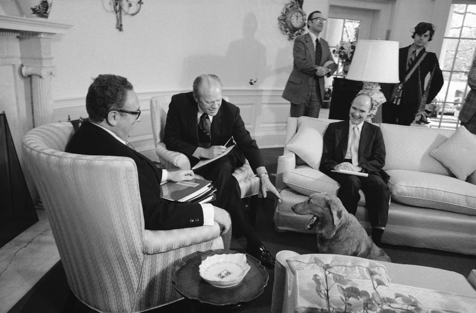 FILE - In this Nov. 16, 1974 file photo, Liberty, President Gerald Ford's golden retriever, receives greetings from the President as he made an unexpected visit to the Oval Office, at the White House in Washington. Liberty dropped by while Ford was meeting with Secretary of State Henry Kissinger and Maj. Gen. Brent Scowcroft, deputy assistant for national security affairs. A longtime adviser to Presidents Gerald Ford and George H.W. Bush has died. Brent Scowcroft was 95. A spokesperson for the late President Bush says Scowcroft died Thursday of natural causes at his home in Falls Church, Virginia.(AP Photo/Charles Tasnadi)