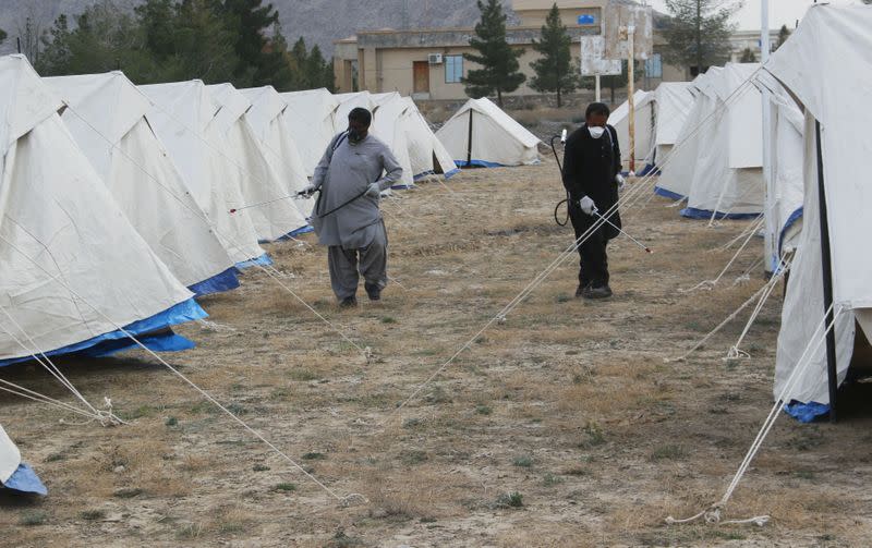 FILE PHOTO: Men with face masks spray near tents setup to quarantine people who cross from Iran border post Taftan, on the outskirts of Quetta